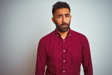 Young indian man wearing red elegant shirt standing over isolated grey background looking sleepy and tired, exhausted for fatigue and hangover, lazy eyes in the morning.