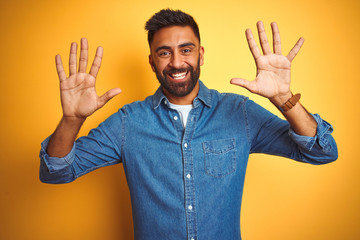 Young indian man wearing denim shirt standing over isolated yellow background showing and pointing...