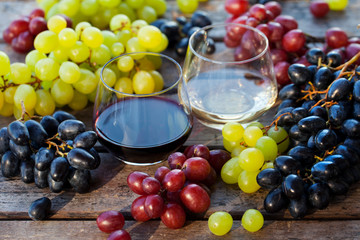 Glass of red and white wine with fresh grape assortment on wooden table. Close up.