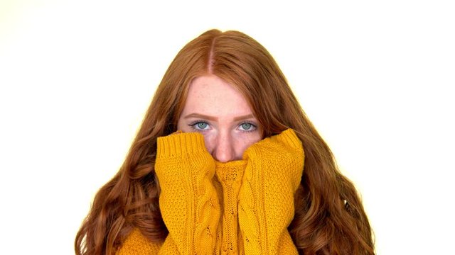 Freezing cute girl hiding cold face behind warm sweater. Slow motion close up.