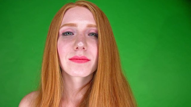 Red haired model girl with make up smiling and kissing with red lips. Green screen close up.
