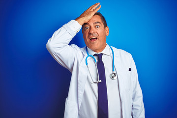 Handsome middle age doctor man wearing stethoscope over isolated blue background surprised with hand on head for mistake, remember error. Forgot, bad memory concept.