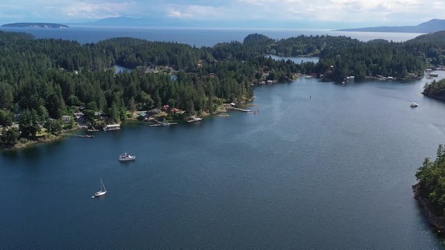 Aerial view over inlet, ocean and island with boat and mountains in beautiful British Columbia. Canada. 4K.