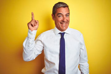 Handsome middle age businessman standing over isolated yellow background pointing finger up with successful idea. Exited and happy. Number one.