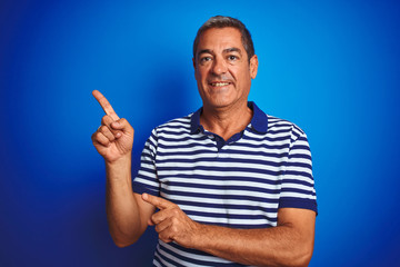 Fototapeta premium Handsome middle age man wearing striped polo standing over isolated blue background smiling and looking at the camera pointing with two hands and fingers to the side.