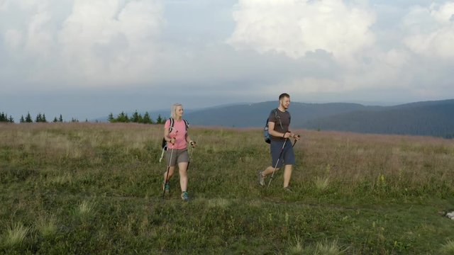 An adventurous backpacker couple hiking/trekking beautiful green mountains during early morning hours with mesmerizing landscape in background. Drone footage.