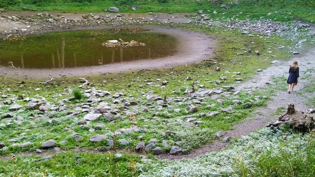 Solo woman discovering the fields of dried up Kaali Crater in Estonia, wide shot 