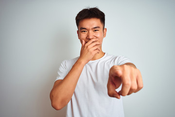 Fototapeta premium Young asian chinese man wearing t-shirt standing over isolated white background laughing at you, pointing finger to the camera with hand over mouth, shame expression