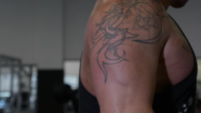 Strong muscular tattooed bodybuilding man doing triceps rope pushdown muscle repetition workout exercise in gym