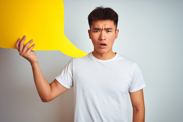 Asian chinese man holding speech bubble standing over isolated white background scared in shock with a surprise face, afraid and excited with fear expression