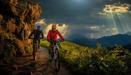 Cycling woman and men riding on bikes at sunset mountains forest landscape. Couple cycling MTB...