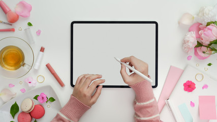 Top view of young girl writing on blank screen tablet in sweet pink feminine workspace