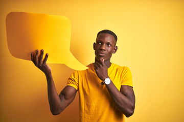 Young african american man holding speech bubble standing over isolated yellow background serious...
