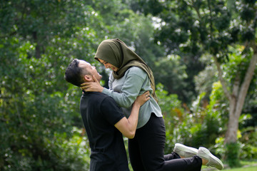 Outdoors photo, beautiful, young muslim couple, hugging and kissing and being affectionate with each other. nature in the background.