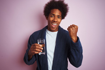 African american man wearing pajama drinking glass of water over isolated pink background screaming...