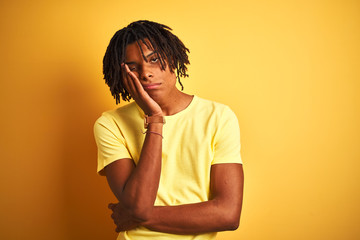 Afro man with dreadlocks wearing casual t-shirt standing over isolated yellow background thinking looking tired and bored with depression problems with crossed arms.