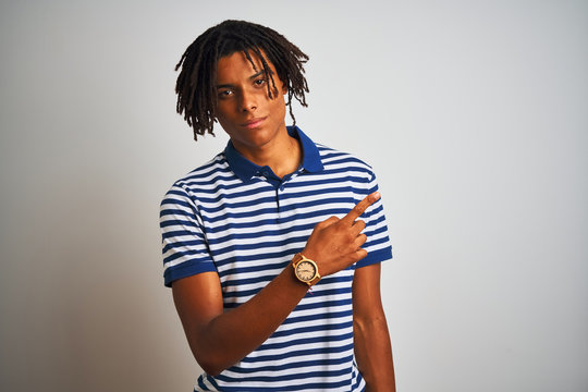 Afro man with dreadlocks wearing striped blue polo standing over isolated white background Pointing with hand finger to the side showing advertisement, serious and calm face