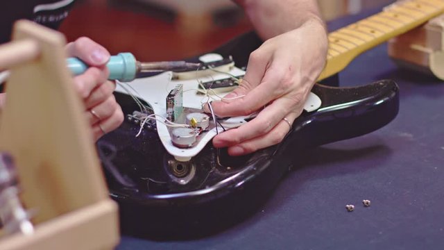 Guitar maker soldering wires of a damaged electric guitar