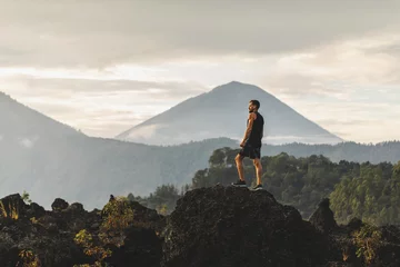 Young man standing on top of stone and enjoying amazing volcanic mountain Agung view in Bali. Travel and active lifestyle concept. © Oleg Breslavtsev