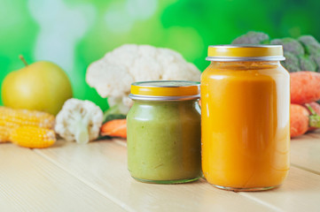 Jars with vegetable puree on the light wooden background