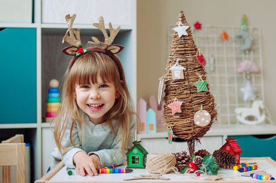 Happy little girl near wooden Christmas tree with handmade corrugated cardboard decorations