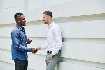 Cheerful male business colleagues shaking hands and greeting each other outside the office building