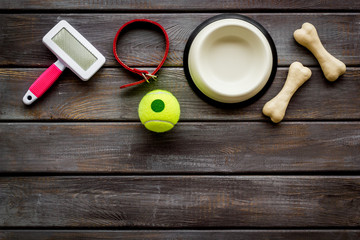 Pet's accessories like bones, collar and bowl on dark wooden background top view flat lay copy space