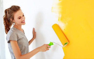 Repair in apartment. Happy young woman paints wall - obrazy, fototapety, plakaty
