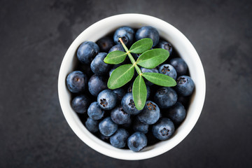 Fresh blueberries in bowl on black background, table top view