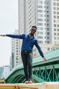 Portrait of young positive Black entrepreneur walking on granite borded in the city