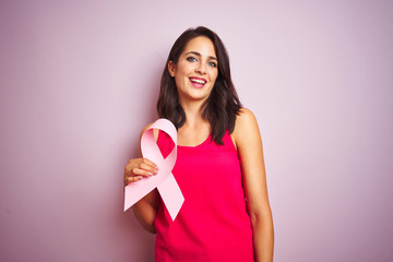 Young beautiful woman holding cancer ribbon over pink isolated background with a happy face standing and smiling with a confident smile showing teeth