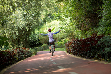 Woman cyclist riding mountain bike on tropical rainforest trail with arms outstretched