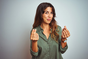 Young beautiful woman wearing green shirt standing over grey isolated background doing money...