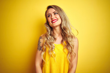 Young beautiful woman wearing t-shirt standing over yellow isolated background looking away to side with smile on face, natural expression. Laughing confident.