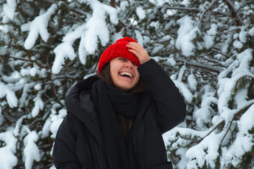 Fototapeta na wymiar portrait of young smiling woman in winter clothes in red hat with bubo fir tree in background