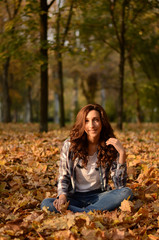 Naklejka na ściany i meble Beautiful girl sitting on the ground in park. Leisure time on warm autumn day. Autumn mood, enjoy the season