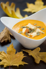Closeup of cream-soup with pumpkin and addition of fried cheese in a white bowl, selective focus, vertical shot