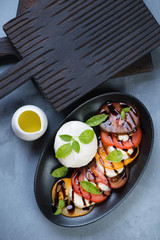 Black plate of caprese salad over grey concrete background, vertical shot, above view