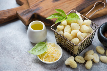 Raw potato gnocchi with green basil leaves, olive oil and grated parmesan over beige stone background