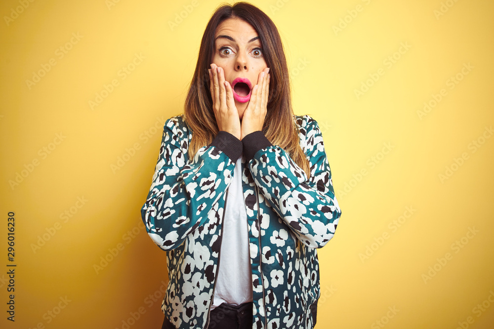 Poster Young beautiful woman wearing casual jacket over yellow isolated background afraid and shocked, surprise and amazed expression with hands on face