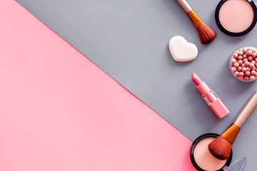 Makeup concept. Frame with decorative cosmetics and brushes on pink and grey background top view copy space