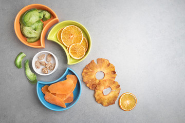 Candied fruits of different tropical fruits in colored plates on a grey stone background .