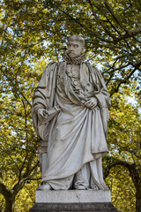 Fototapeta premium Statue of Michel de Montaigne in public garden along Place des Quinconces, Bordeaux France, with a canopy of green trees.