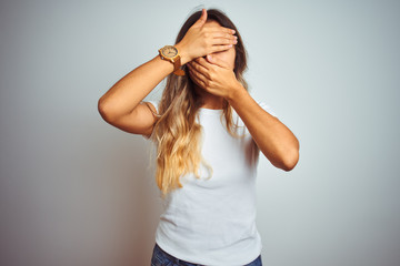 Young beautiful woman wearing casual white t-shirt over isolated background Covering eyes and mouth with hands, surprised and shocked. Hiding emotion