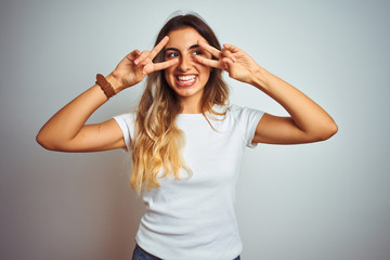 Young beautiful woman wearing casual white t-shirt over isolated background Doing peace symbol with...