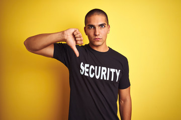 Young safeguard man with security t-shirt over yellow isolated background with angry face, negative...