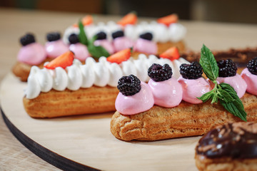 Traditional French dessert. Eclair with cream, strawberries, cherry, mint on wooden background selective focus