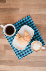 Hot coffee cup and croissant on wooden table background.Cafe drinking menu espresso and latte art at the restaurant.Breakfast menu in the morning time.