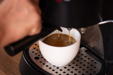 Selective focus white cup for fresh hot coffee in the morning time at home.Woman hand making coffee with coffee machine on wooden counter.