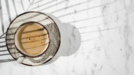 A white filled with coffee cup on a white background covered by a ficus leaf shadow